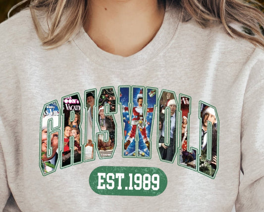 A person wearing a gray sweatshirt with a vintage Christmas collage design, featuring various cartoon characters and text that reads 'GRISTWOOD EST. 1989'.