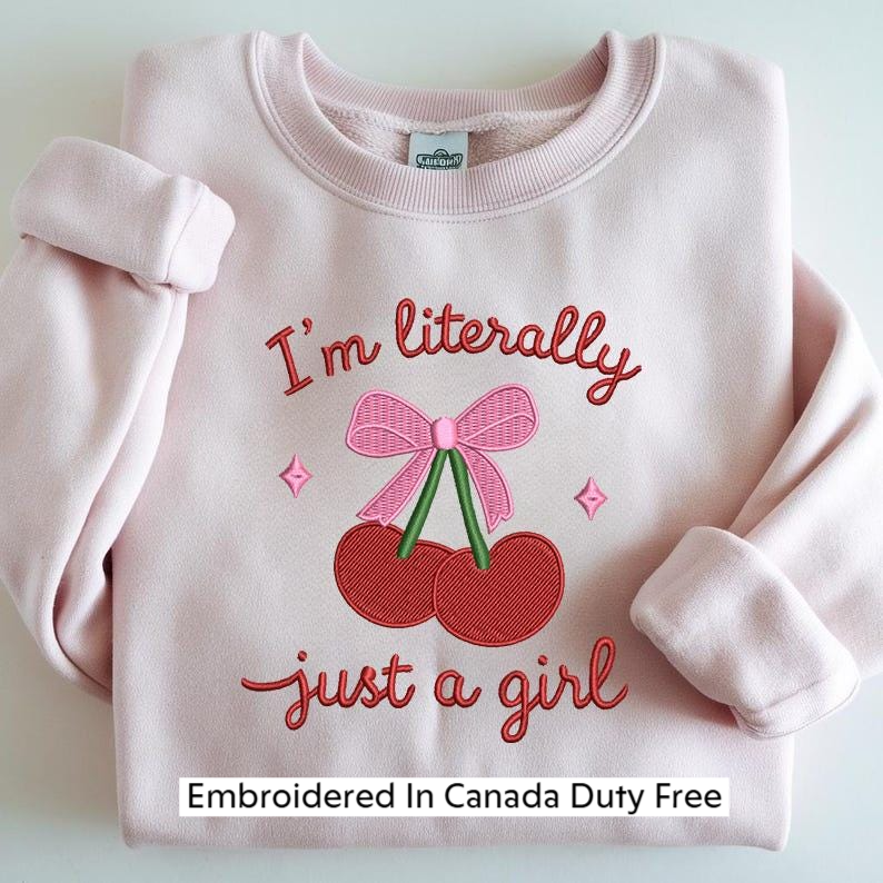 A pink sweater with a red bow and the text "I'm literally just a girl" embroidered on it.