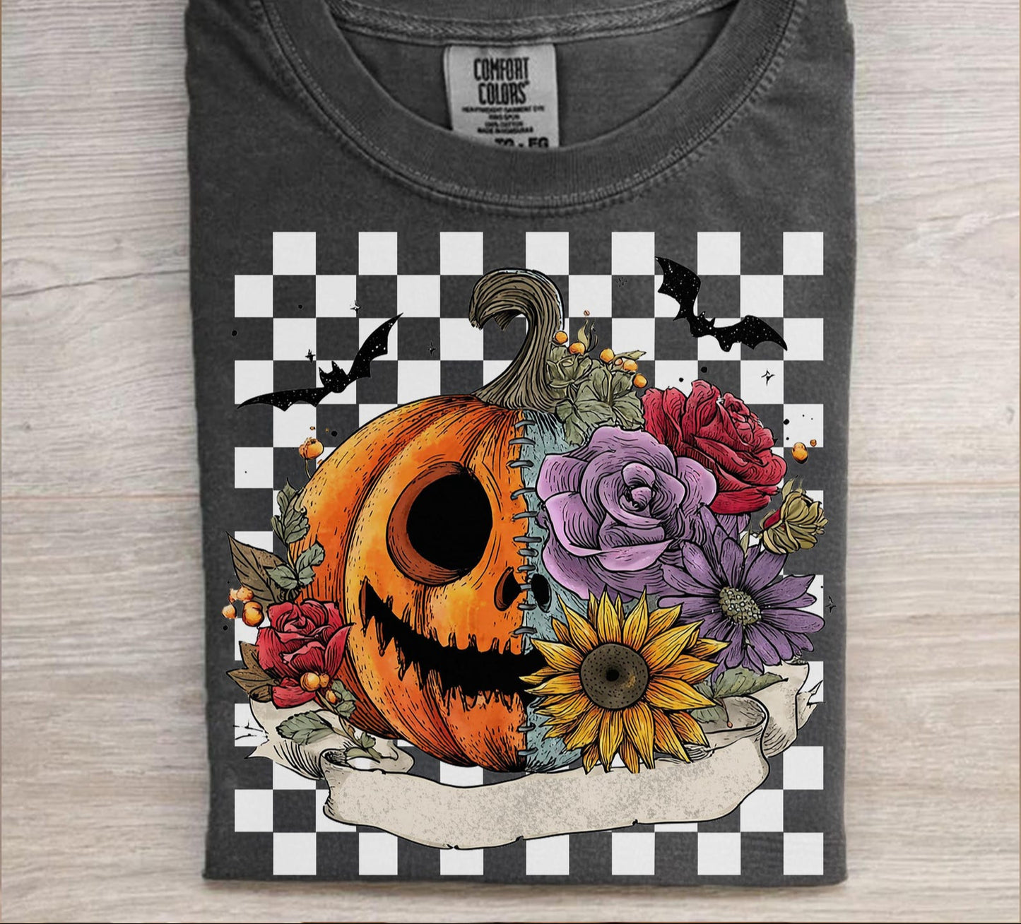 Gray t-shirt with a Halloween-themed design featuring a pumpkin, flowers, and bats on a checkered background.