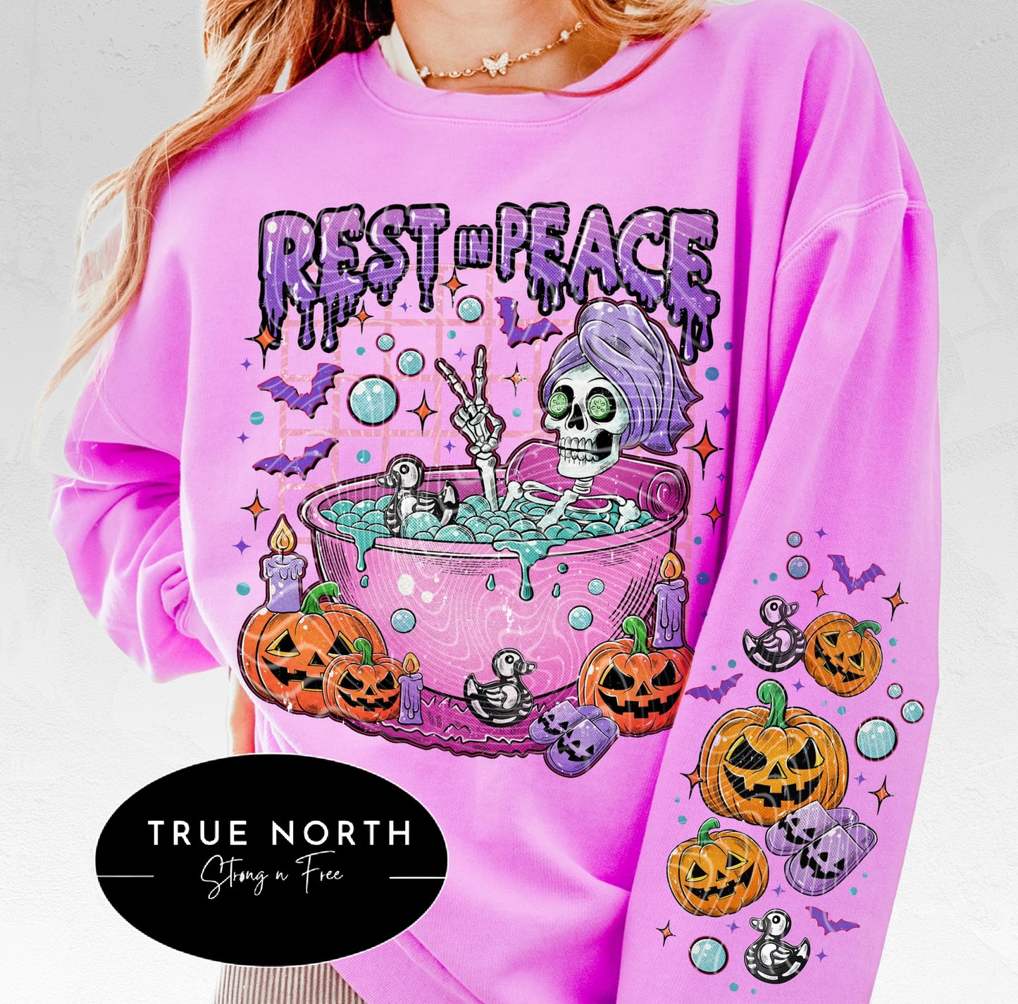 A pink sweatshirt with 'Rest in Peace' text and a Halloween-themed graphic design featuring a skull, pumpkins, and bats.