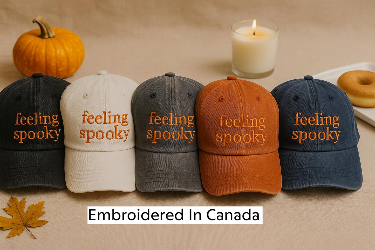 a collection of five baseball caps with the word "spooky" embroidered on them, arranged in a row on a table. In addition to the caps, there is a lit candle, a donut, and a pumpkin, creating a spooky and autumnal atmosphere.