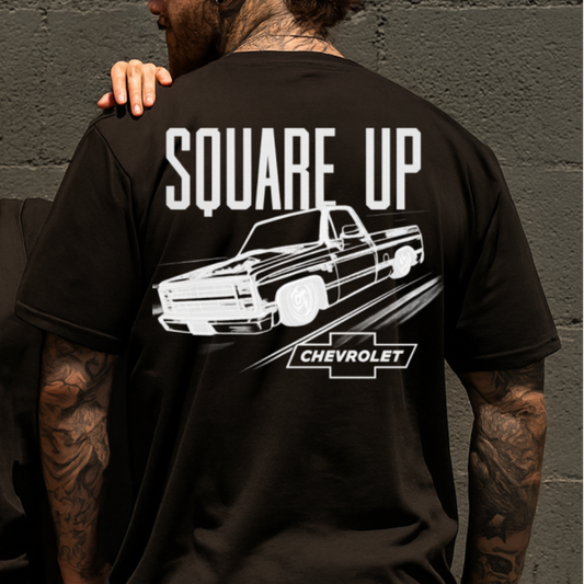 Two people wearing black t-shirts with 'Square Up Chevrolet' graphic design against a gray wall.