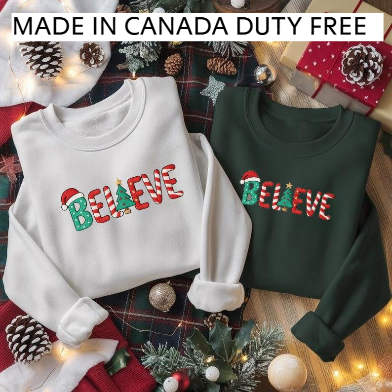 two Christmas-themed sweatshirts, one white and one green, with the word "Believe" printed on them. The sweatshirts are displayed on a plaid blanket, surrounded by Christmas decorations such as pine cones, ornaments, and a Christmas tree. The image also includes text that reads "MADE IN CANADA DUTY FREE".