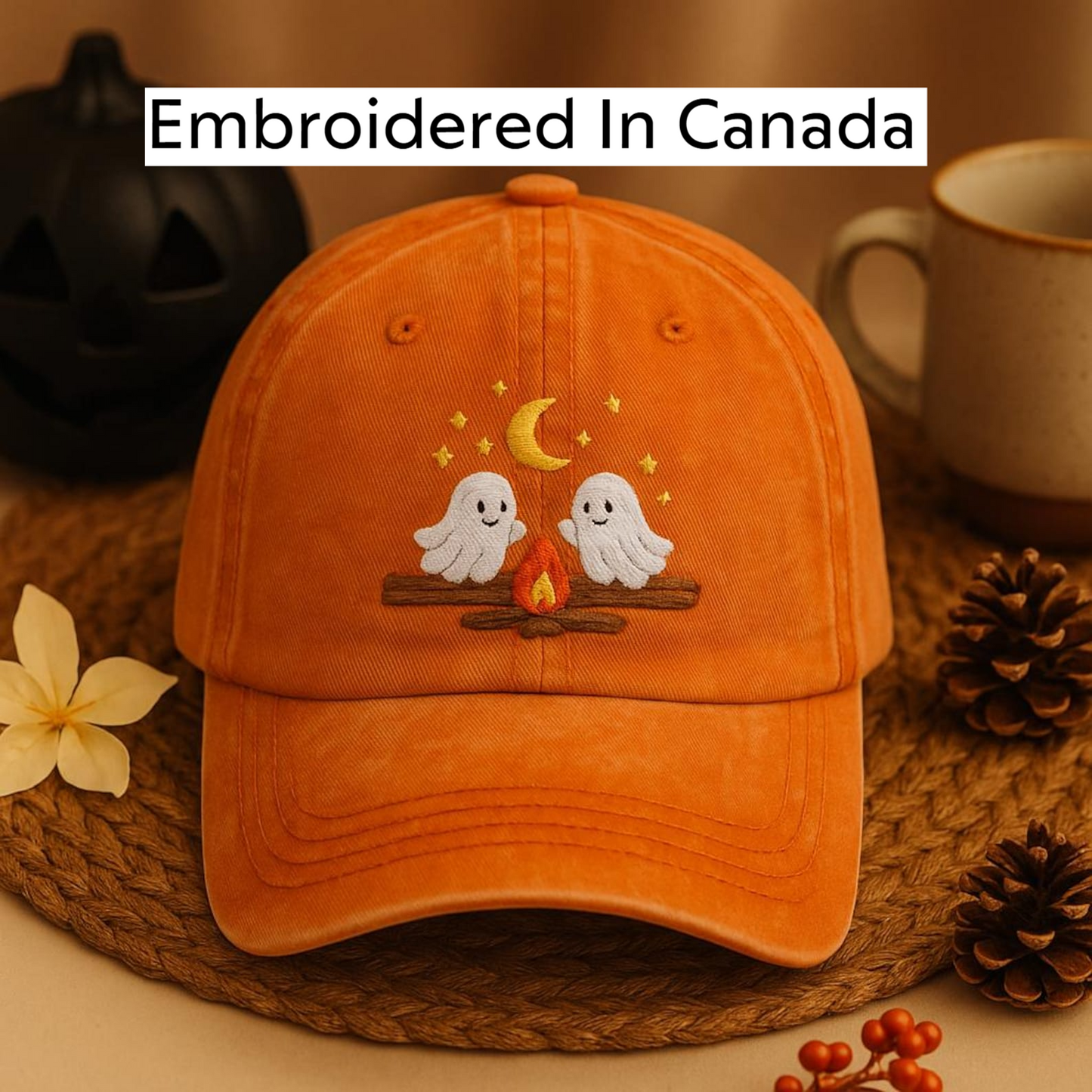 An orange baseball cap with a Halloween-themed embroidered design, featuring two ghostly figures and a crescent moon, placed on a woven mat.