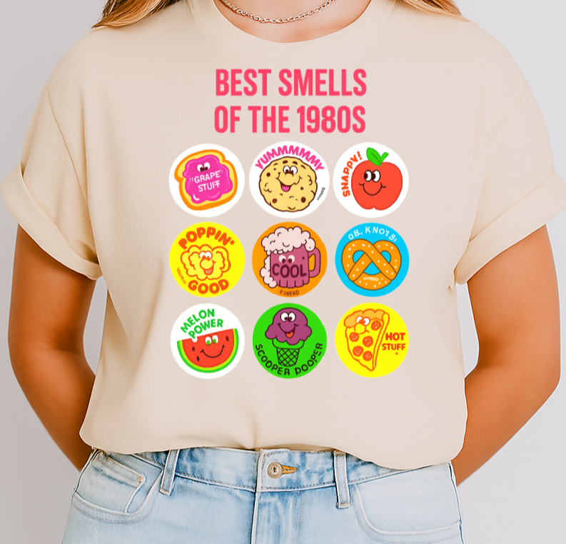 Person wearing a beige t-shirt with colorful graphic designs and text on a plain background