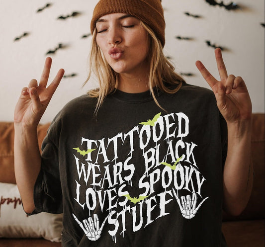 Person wearing a black t-shirt with text and making peace signs, with a Halloween-themed background.