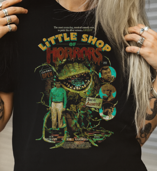 Person wearing a black 'Little Shop ' t-shirt with a graphic design.