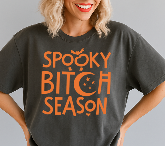 Person wearing a dark gray t-shirt with 'Spooky Bitch Season' text and a black cap on a gray background