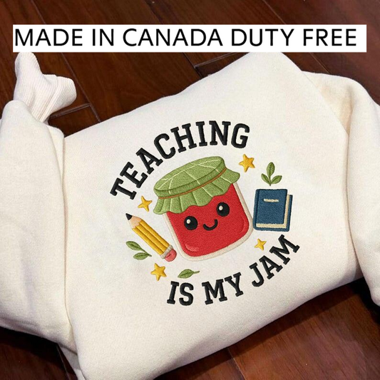 A white sweatshirt with a colorful embroidered design that says "Teaching is my jam" and features a smiling red character with a green hat and a pencil.
