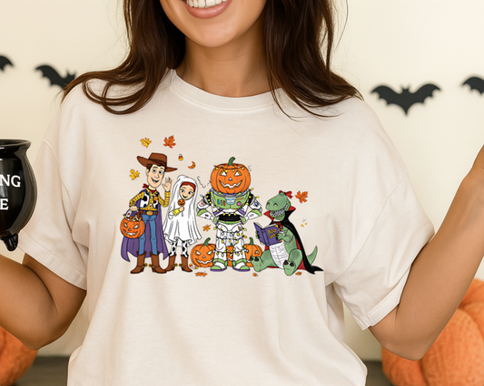 Person wearing a Halloween-themed t-shirt with cartoon characters and holding a mug, surrounded by pumpkins and decorative bats.