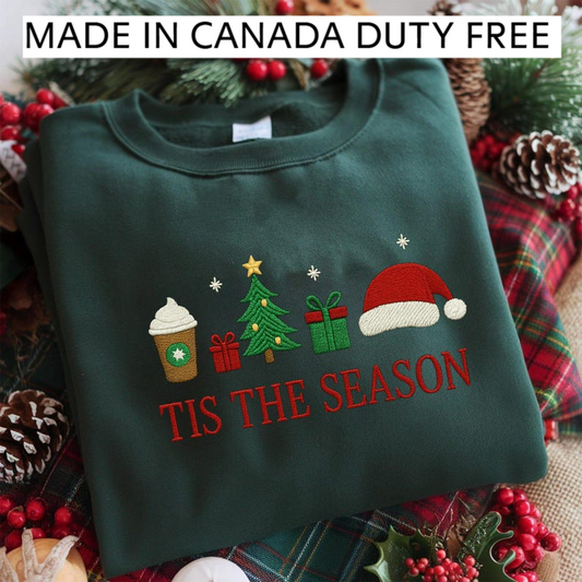 A green sweater with a Christmas-themed embroidered design, including a coffee cup, a Christmas tree, a gift box, and a Santa hat, along with the text "TIS THE SEASON" printed on it.