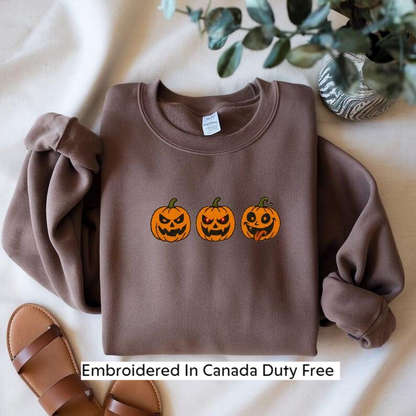 A brown sweater with a Halloween-themed design of three jack-o'-lanterns, along with a pair of sandals and a potted plant, all laid out on a white surface.