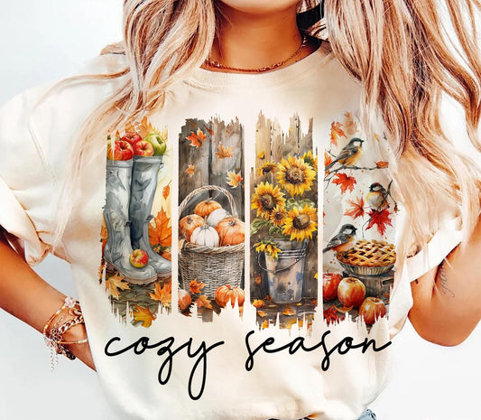 Person wearing a white t-shirt with autumn-themed design and 'cozy season' text.