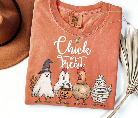 Folded orange t-shirt with Halloween-themed chicken illustrations and text on a white background.
