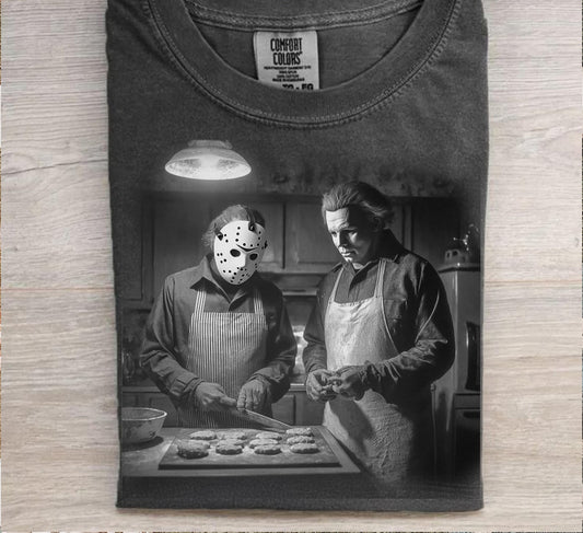 Black t-shirt with a graphic of two people in a kitchen, one wearing a hockey mask, on a wooden surface.