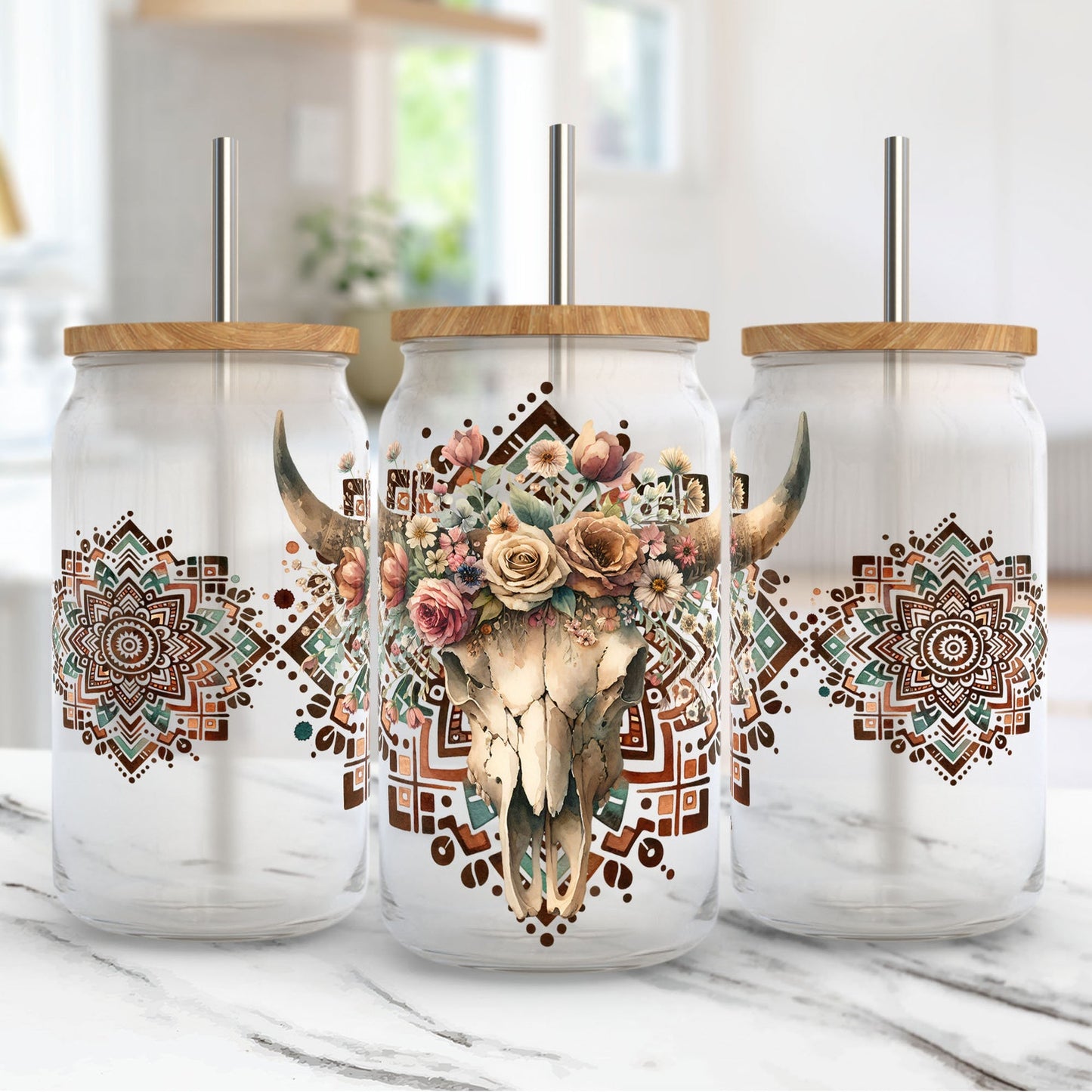 Three glass tumblers with cow skull and floral design on a marble surface.