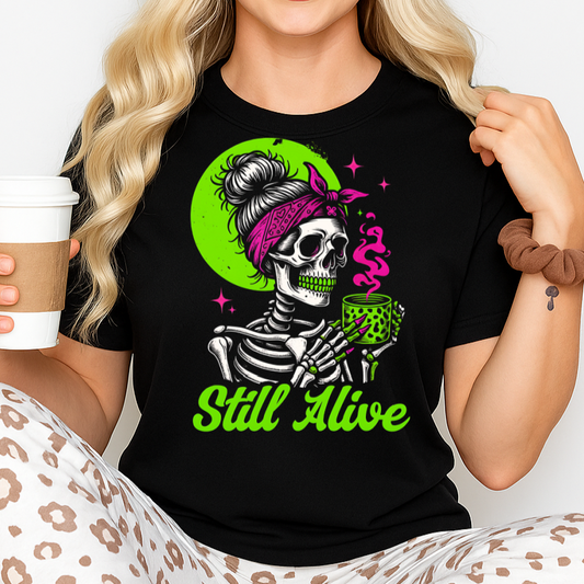 Person wearing a black t-shirt with a skeleton design and 'Still Alive' text, holding a coffee cup.