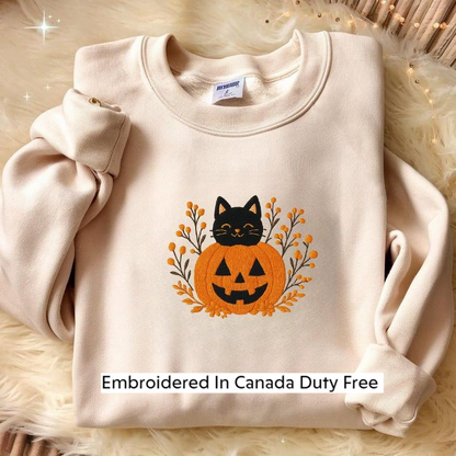 A beige sweater with a Halloween-themed embroidered pumpkin and cat design, along with the text "Embroidered In Canada Duty Free".