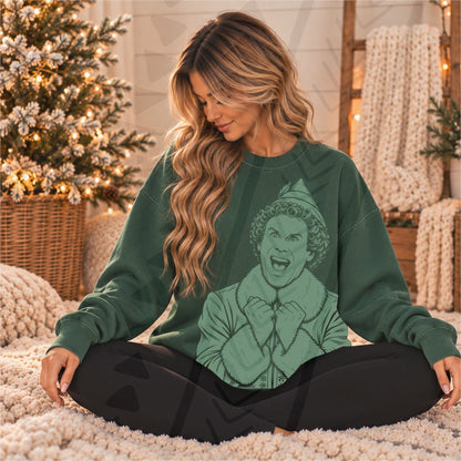 Green Buddy the Elf portrait with excited expression, elf hat and raised hands, shown on a forest-green sweatshirt; DTF transfer only, garment not included.