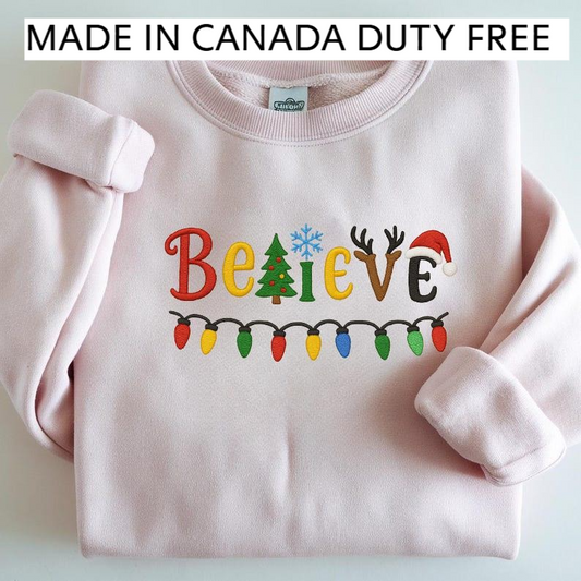 A pink sweatshirt with the word "Believe" embroidered on it, along with Christmas-themed elements such as a snowflake, reindeer, and Christmas lights.