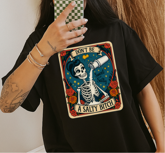 Person wearing a black t-shirt with a graphic design and text, holding a phone.