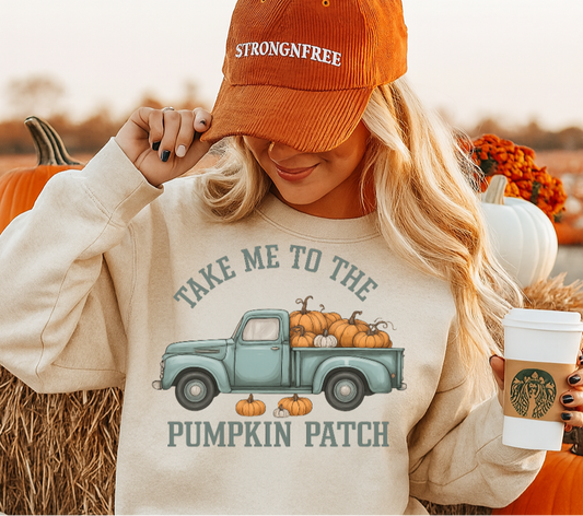 Woman wearing a sweatshirt with a pumpkin patch graphic and an orange cap, sitting in a pumpkin patch.