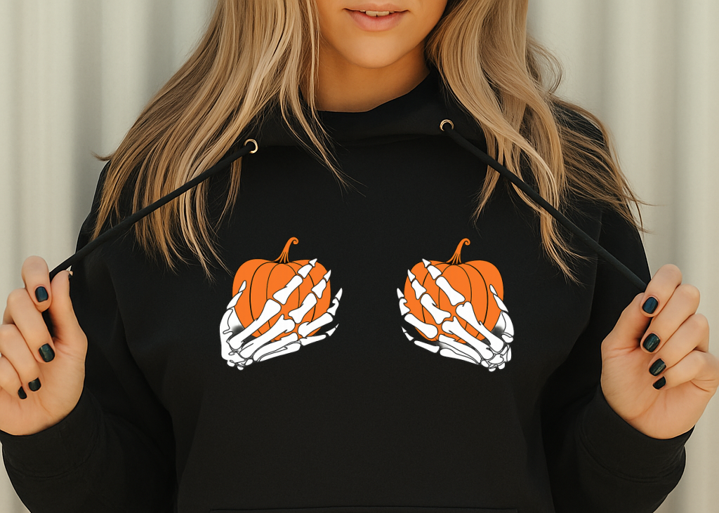 Person wearing a black hoodie with pumpkin and skeleton hand design on a neutral background