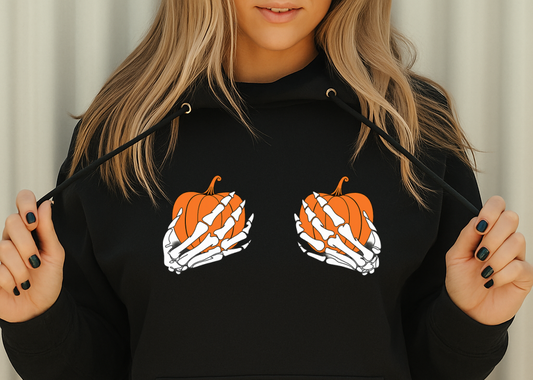 Person wearing a black hoodie with pumpkin and skeleton hand design on a neutral background