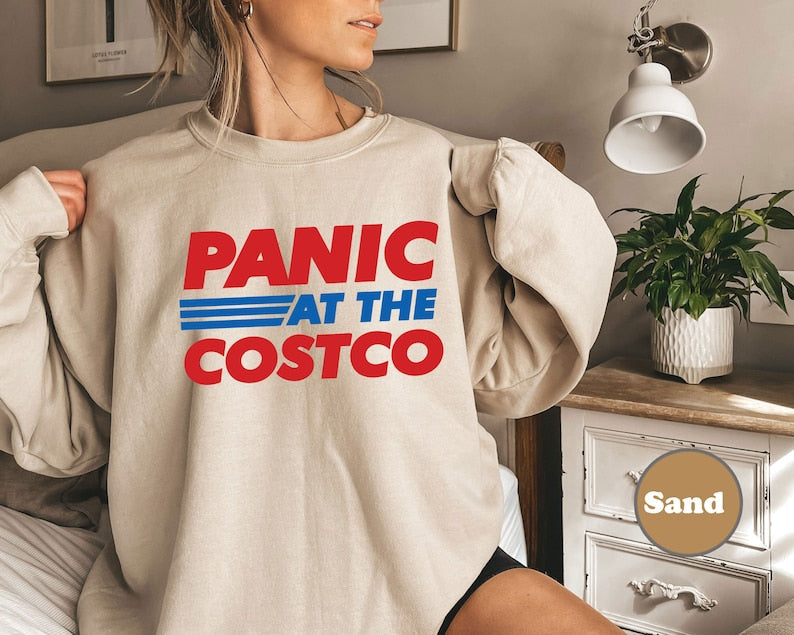 a woman sitting on a bed wearing a sweatshirt that says panic at the costco